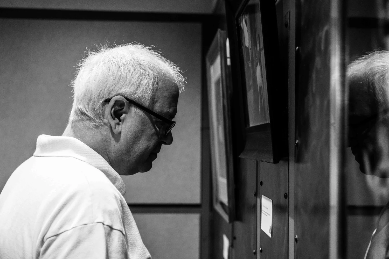 A man with white hair and glasses looking at display screens mounted on a wooden wall.