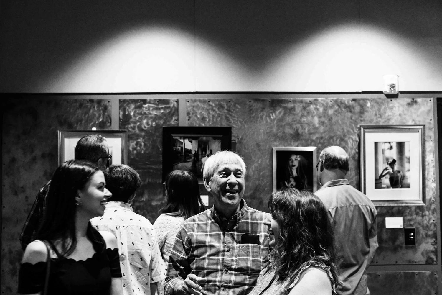 People at an art gallery socializing and viewing framed artworks on the wall.