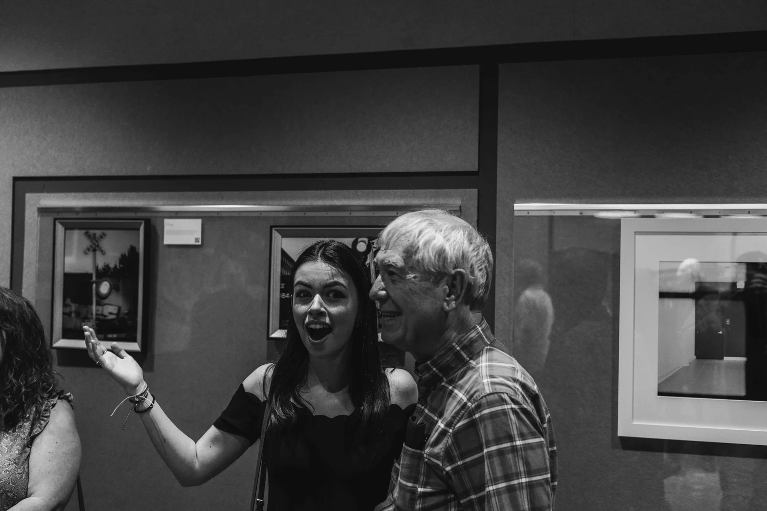 Two women, one with dark hair and one with gray hair, talking and smiling at an art gallery or museum.